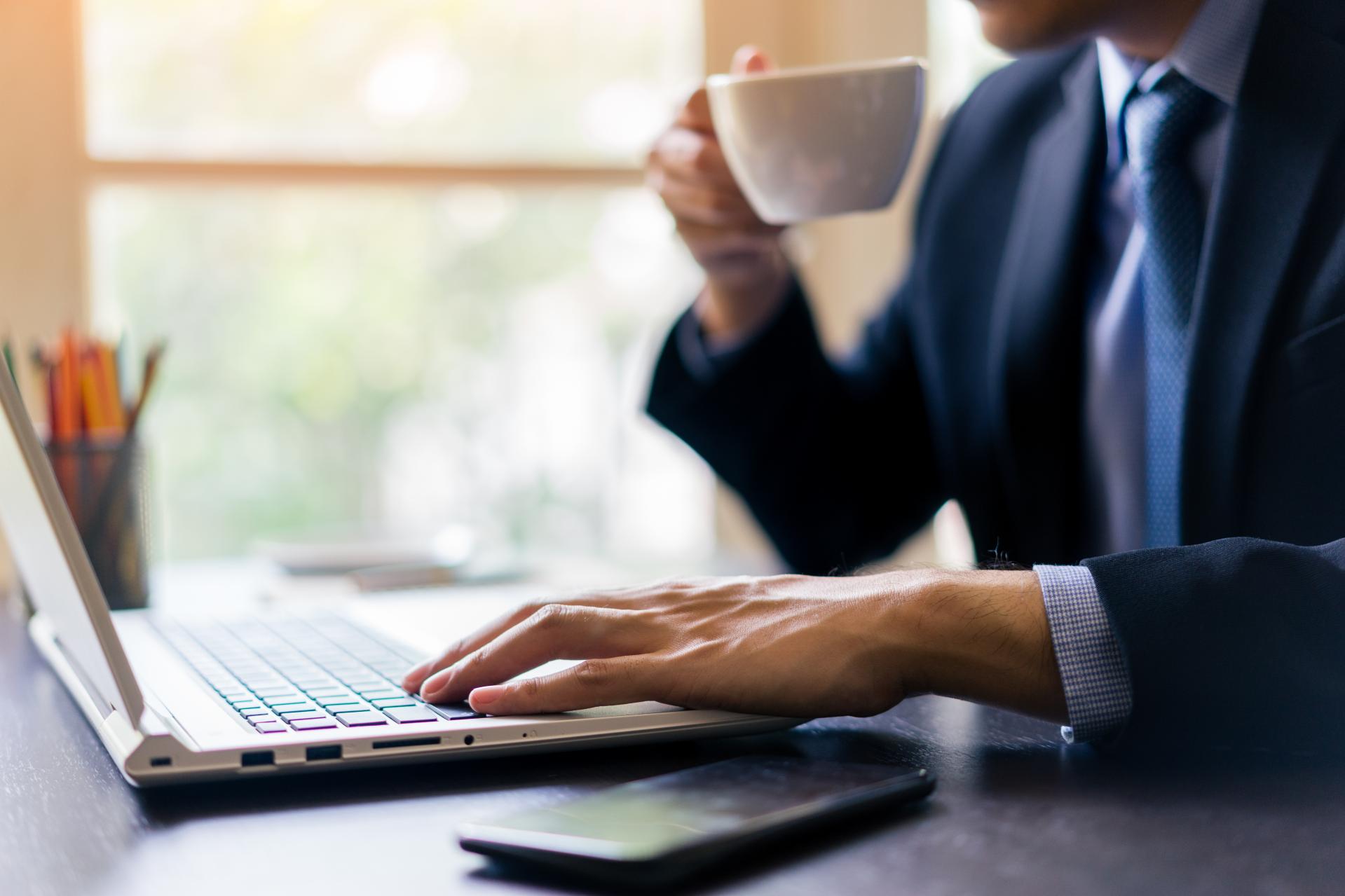 Man drinking coffee in front of laptop